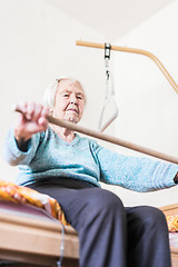 Image showing Elderly 96 years old woman exercising with a stick sitting on her bad.