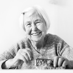 Image showing Cheerful elderly 96 years old woman sitting at table at home happy with her pension savings in her wallet after paying bills. Black and white.