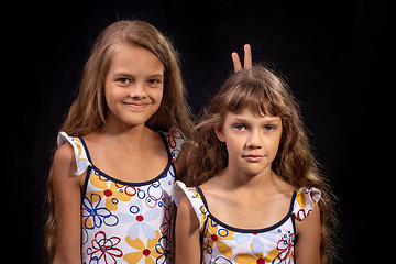 Image showing The older sister put the little horns, a portrait on a black background