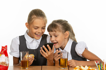 Image showing Two schoolgirls at a break watching a video on the phone, and eating liver and orange, drinking juice