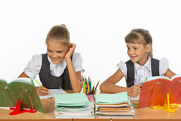 Image showing Two schoolgirls are sitting at a desk and cheerfully looking at the textbook