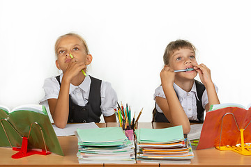 Image showing Two schoolgirls pensively and funny sit at the table and look up