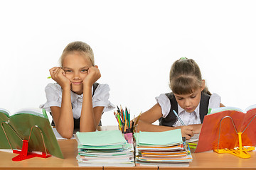 Image showing Two schoolgirls at a desk, one leaning on her hands and looking into the frame, the other writes