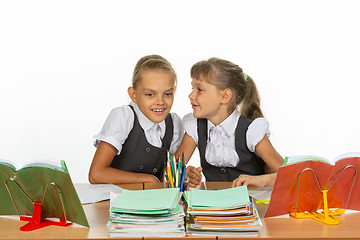 Image showing Two girls whisper while sitting at a desk