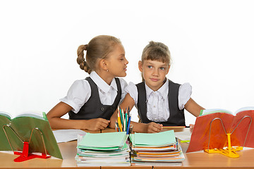 Image showing Girls are sitting at a school desk, one whispers to the other something in the ear