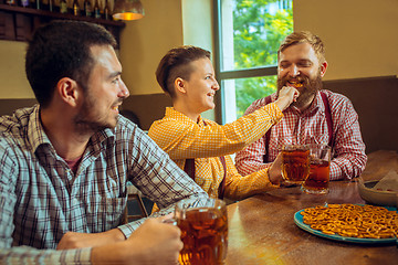 Image showing people, leisure, friendship and communication concept - happy friends drinking beer, talking and clinking glasses at bar or pub