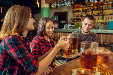 Image showing people, leisure, friendship and communication concept - happy friends drinking beer, talking and clinking glasses at bar or pub