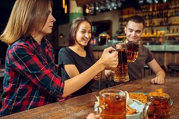 Image showing people, leisure, friendship and communication concept - happy friends drinking beer, talking and clinking glasses at bar or pub