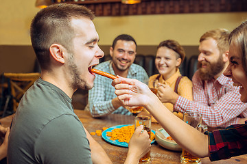 Image showing people, leisure, friendship and communication concept - happy friends drinking beer, talking and clinking glasses at bar or pub