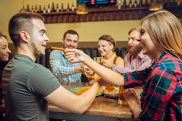 Image showing people, leisure, friendship and communication concept - happy friends drinking beer, talking and clinking glasses at bar or pub