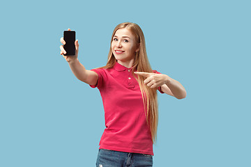 Image showing Portrait of a confident casual girl showing blank screen mobile phone isolated over blue background