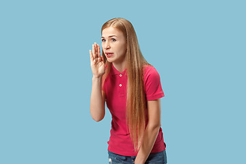 Image showing The young woman whispering a secret behind her hand over blue background