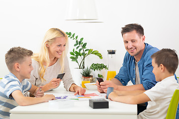 Image showing Happy young family playing card game at dining table at bright modern home.