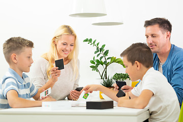 Image showing Happy young family playing card game at dining table at bright modern home.