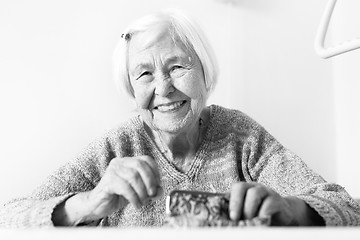 Image showing Cheerful elderly 96 years old woman sitting at table at home happy with her pension savings in her wallet after paying bills. Black and white.