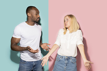 Image showing Beautiful female and male portrait on pink and blue studio backgroud. The young emotional couple