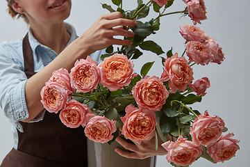 Image showing Florist girl in a brown apron holding a vase with pink roses on 