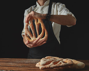 Image showing on background of wooden brown table, men\'s hands hold bread fougas