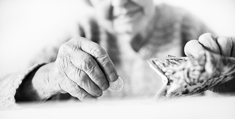 Image showing Detailed closeup photo of unrecognizable elderly womans hands counting remaining coins from pension in her wallet after paying bills. Black and white image.