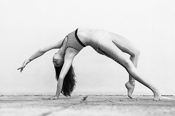 Image showing Fit sporty active girl in fashion sportswear doing yoga fitness exercise in front of gray wall, outdoor sports, urban style. Black and white photo.