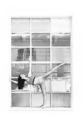 Image showing Fit sporty active girl in fashion sportswear doing yoga fitness exercise in front of big industrial window frame. colorful reflections in window glass. Urban style yoga. Black and white