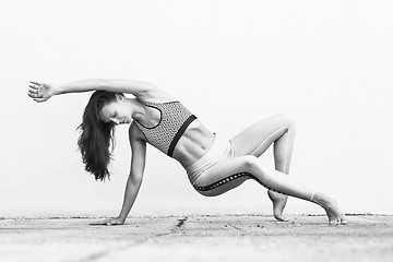 Image showing Fit sporty active girl in fashion sportswear doing yoga fitness exercise in front of gray wall, outdoor sports, urban style. Black and white photo.