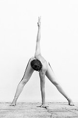 Image showing Fit sporty active girl in fashion sportswear doing yoga fitness exercise in front of gray wall, outdoor sports, urban style. Black and white photo.