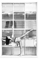 Image showing Fit sporty active girl in fashion sportswear doing yoga fitness exercise in front of big industrial window frame. colorful reflections in window glass. Urban style yoga. Black and white