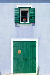 Image showing Cute retro purple house with green wooden window with shutters and flowers in the pot and green door with white frame.