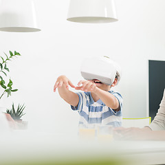 Image showing Amazed child using virtual reality headsets trying to grab unexisting virtual objects while sitting at the dinner table.