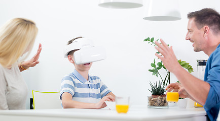 Image showing Happy caucasian family at home at dinning table, having fun playing games using virtual reality headset