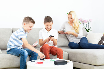 Image showing Brothers playing card game on living room sofa at home supevised by their mother.