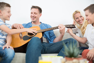 Image showing Happy caucasian family smiling, playing guitar and singing songs together at cosy modern home