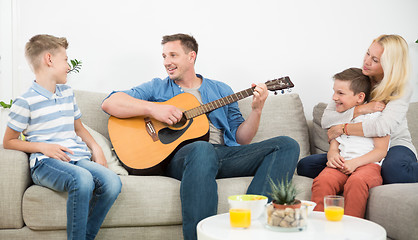 Image showing Happy caucasian family smiling, playing guitar and singing songs together at cosy modern home