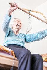 Image showing Elderly 96 years old woman exercising with a stick sitting on her bad.