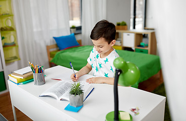 Image showing student boy with book writing to notebook at home