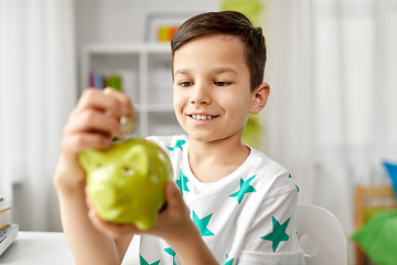 Image showing little boy putting coin into piggy bank at home