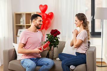 Image showing happy man giving woman flowers and present at home