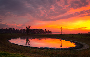 Image showing Windmill by pond in rural field with vivid sunrise