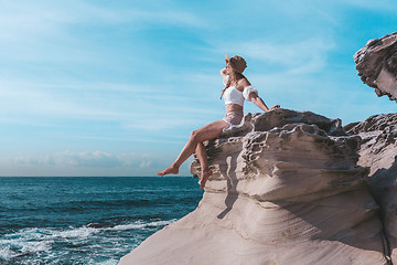 Image showing Female enjoying summer sunshine, Sitting by ocean wearing sunhat