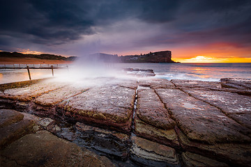 Image showing Sunrise sky and waves crash onto rocky beach shore