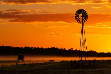 Image showing Silhouette of windmill on farmland against orange yellow sky