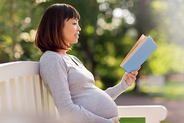 Image showing happy pregnant asian woman reading book at park