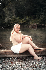 Image showing Young curvy woman sits scantily clad on a lake on a tree trunk