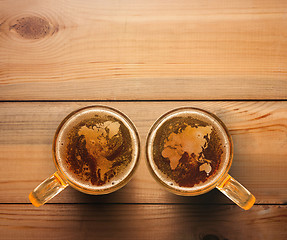 Image showing world map silhouette on foam in beer glass on wooden table.