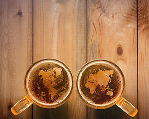 Image showing world map silhouette on foam in beer glass on wooden table.