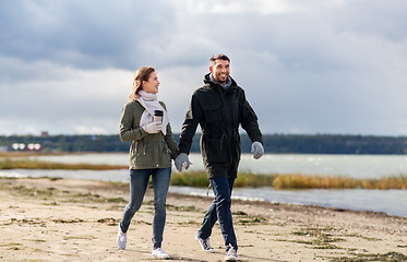 Image showing couple with tumbler walking along autumn beach