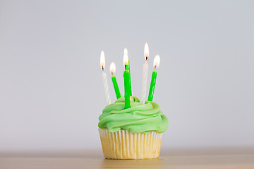 Image showing green cupcake with six burning candles on table