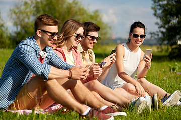 Image showing smiling friends with smartphones sitting on grass