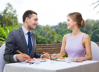 Image showing smiling couple eating sushi rolls at restaurant